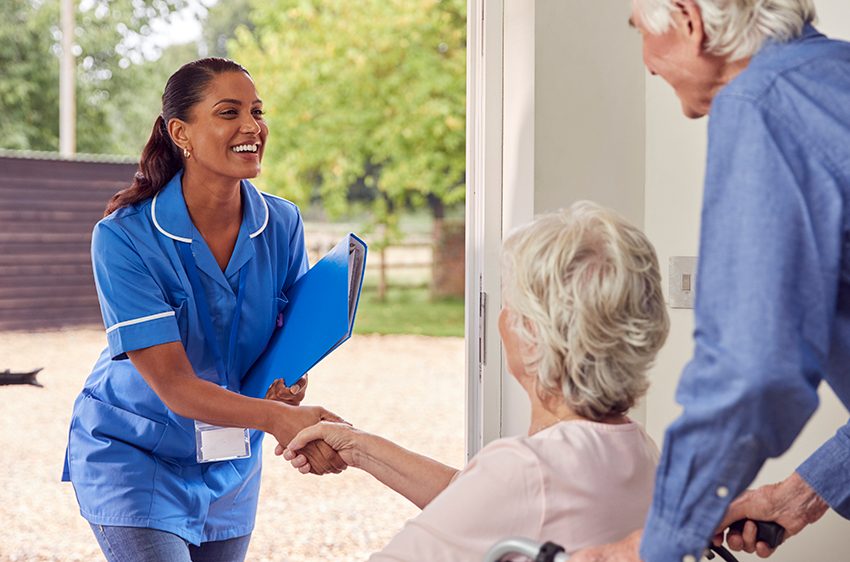 Elderly husband and wife greet female nurse at their door