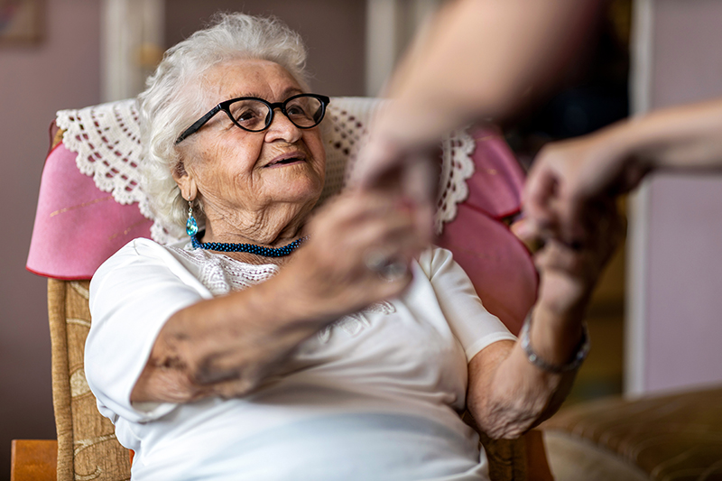 Seated elderly woman smiling and holding hands with health aid